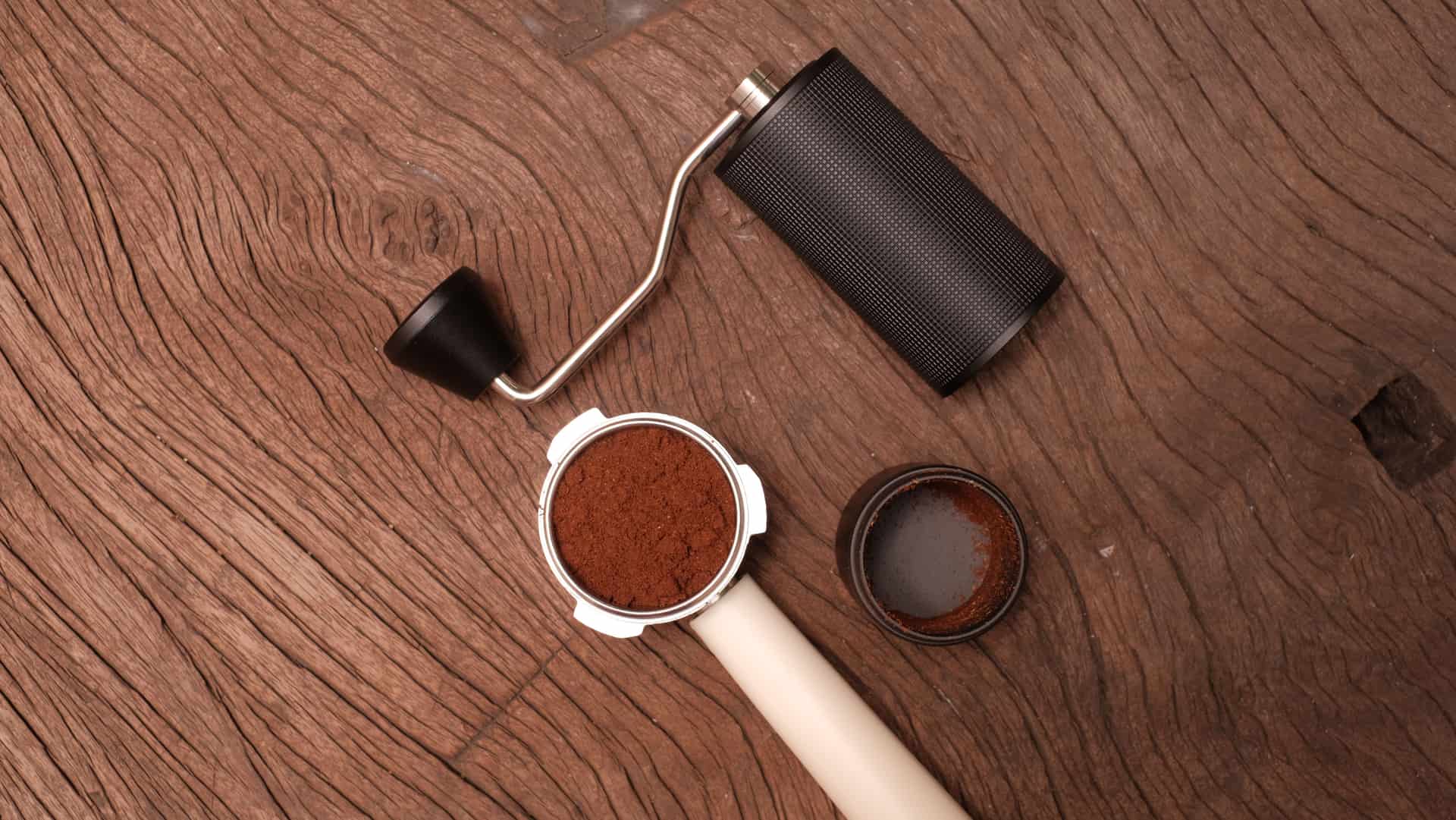 Espresso tools laid out on dark wood: tamper, distribution tool and portafilter